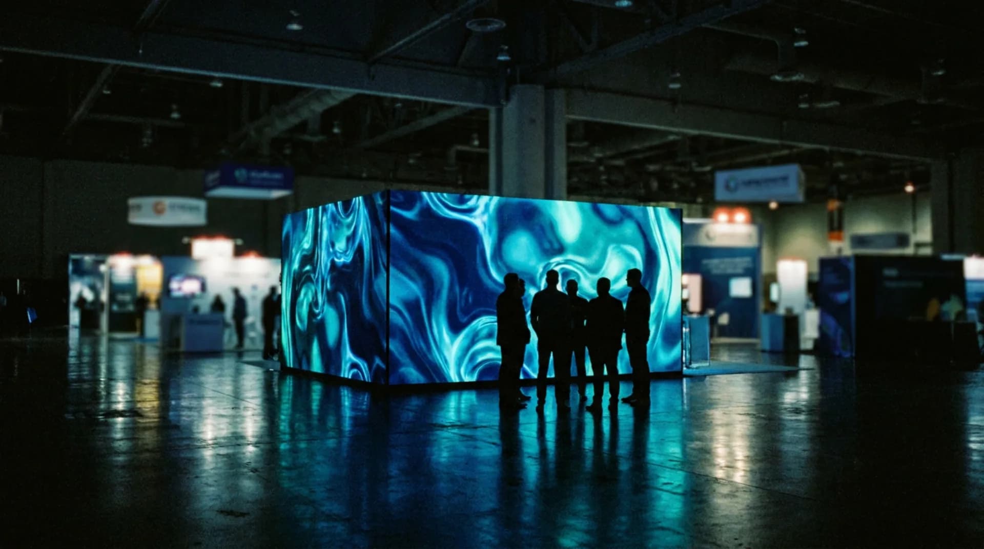 A trade-show booth with a bright LED wall, drawing a small crowd of silhouettes