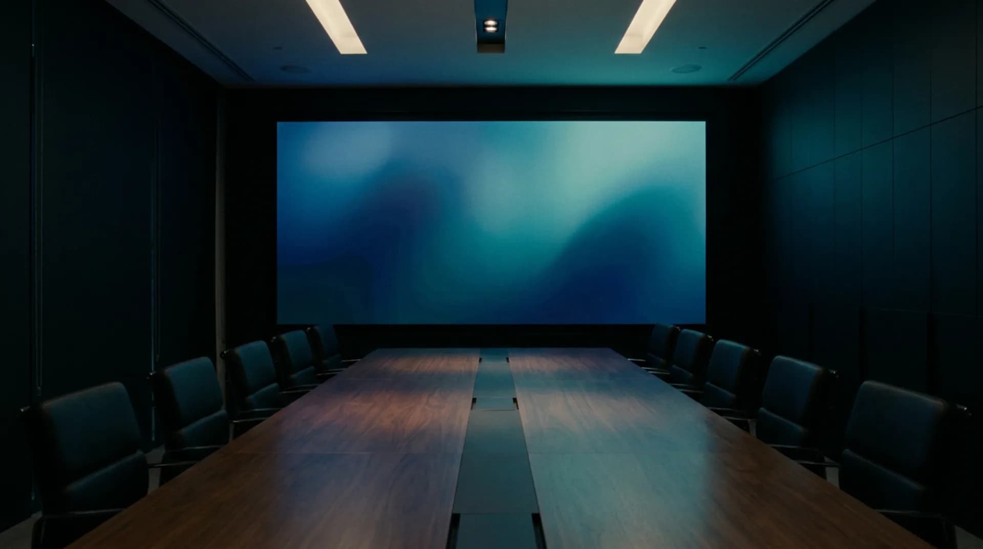 A wide LED wall on the end wall of a boardroom, showing a muted blue gradient above an empty conference table