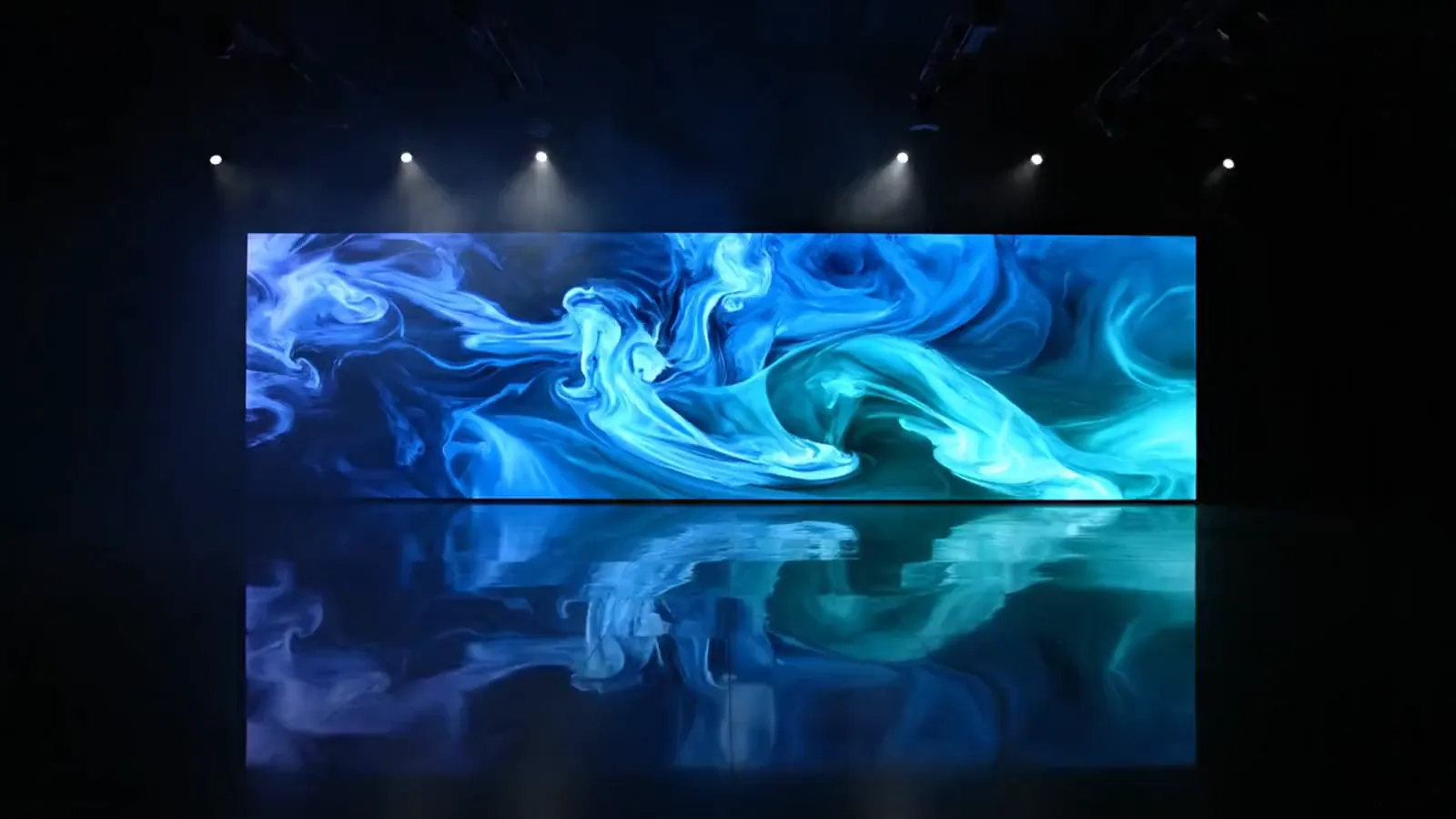 A wide LED video wall in a dark showroom, glowing with slow-moving blue and teal light, reflected on the floor